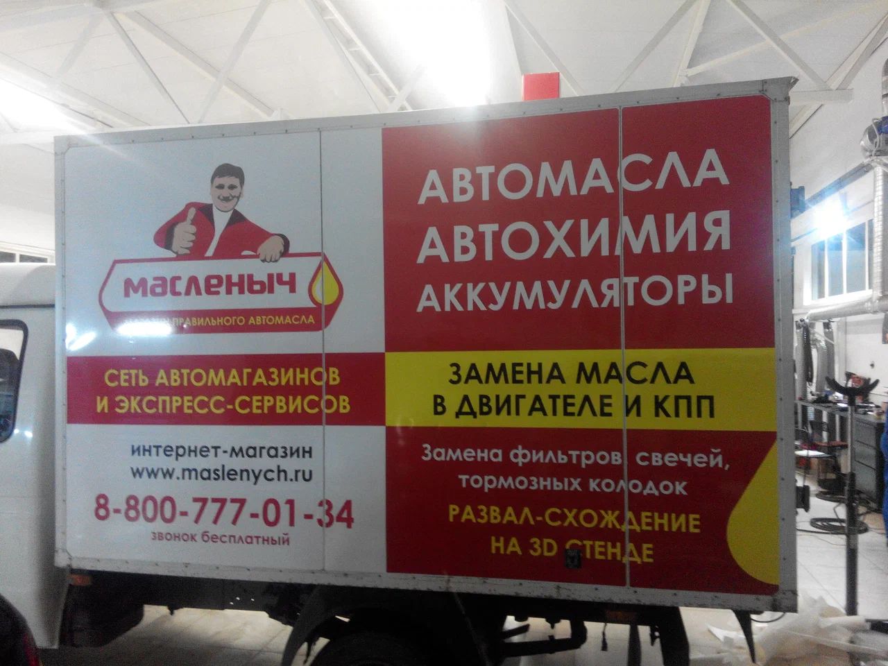 Боковая часть фургона с красно-жёлтой рекламной графикой «Масленыч» и перечнем автомобильных товаров и услуг