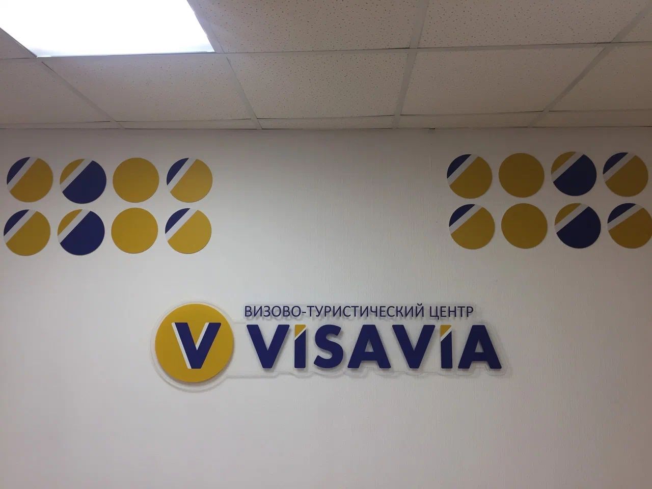 Интерьерная вывеска VISAVIA с круглым жёлтым знаком и сине-жёлтыми элементами на стене